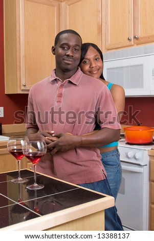 Attractive young african american couple standing in their kitchen with a neutral expression on their faces. She is standing behind him and hugging him. Vertically framed shot.