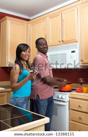 Attractive smiling young African American couple cooking dinner together and drinking red wine.  Vertically framed shot with the man and woman looking towards the camera.