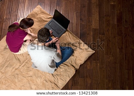 Couple sitting on the floor looking at a laptop screen together. Horizontally framed shot taken from above the subjects.