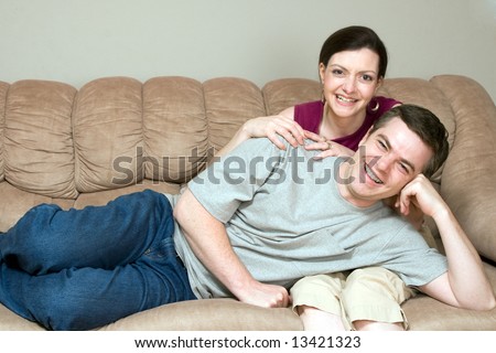 Loving couple relaxing on their couch together. He is lying on her lap. Both are looking at the camera with a smile on their faces. Horizontally framed shot.