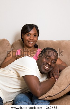 Happy, attractive couple share a couch. Both are smiling and he is lying across her lap. Vertically framed photograph.