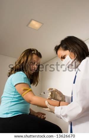 Female Doctor wearing a mask gives a young girl sitting on an examining table a shot. The girl looks scared. Vertically framed photograph
