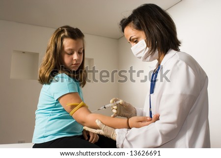 Female Doctor wearing a mask gives a shot to a  young girl who is sitting on an examining table looking nervous. Horizontally framed photograph