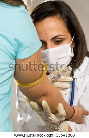 Female Doctor wearing a mask stares intently while she gives a shot to an arm with a tournicate on it. Vertically framed photograph