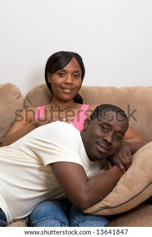 Happy, attractive couple share a couch. Both are smiling and he is lying across her lap. Vertically framed photograph. Vertically framed photograph