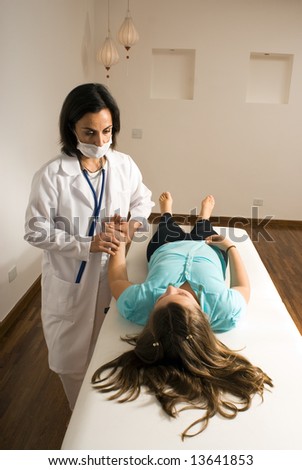 Female doctor wearing a mask checks the pulse of a girl lying down on an examining table. Vertically framed photograph