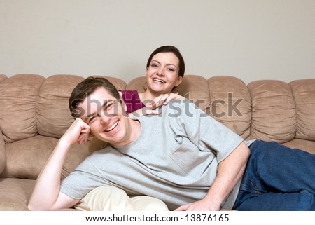 Smiling, happy couple sitting on a couch. They are laughing as he lays across her lap. Horizontally framed photograph