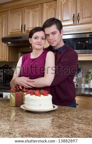 Happy couple hugging in a kitchen near a cake and a present. Vertically framed photograph.