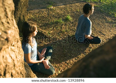 Man and woman practice yoga under large shady trees. Horizontally framed photograph