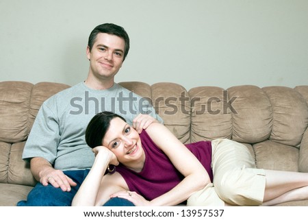 A smiling woman lying on a smiling man\'s lap sitting on a sofa.