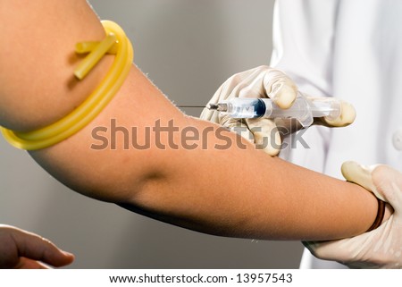 A nurse drawing blood from a patient\'s right arm.  Horizontally framed close-up shot.
