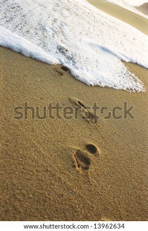 White tide washing over a foot print covered beach.