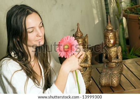 Woman Gazes at Pink Daisies. There  are two bronze statues behind her. Horizontally framed photograph