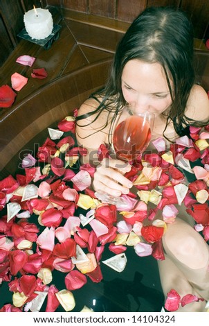 Woman relaxes in a spa tub filled with flowers sips red wine. Vertically framed photograph