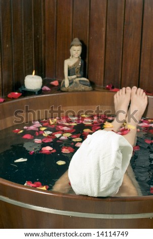 Picture of the back of a woman's head soaking in a tub filled with flower petals. Vertically framed photograph
