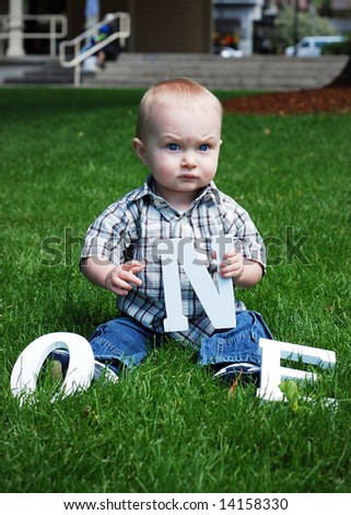 A baby sitting in grass holding a letter N. - vertically framed