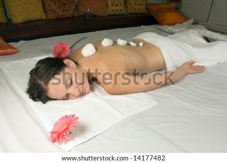 A young girl lying down on a white towel with pink flowers near her, hot rocks are on her back. - horizontally framed