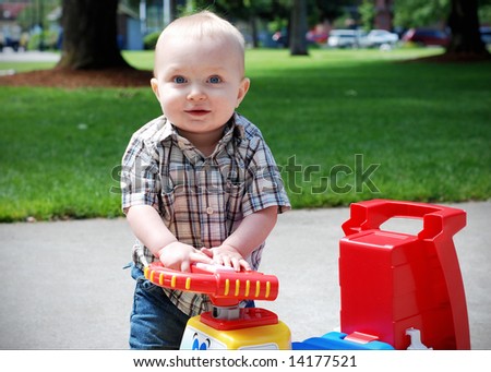 A young child holding onto the steering wheel of a toy truck, smiling. - horizontally framed