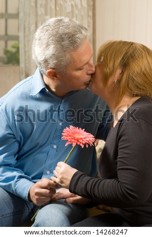 Romantic couple kissing on a couch, holding a bright flower. vertically framed shot.
