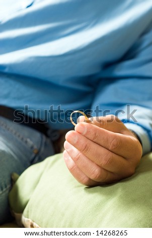 Abstract photo of a Man seated, holding a wedding band in his fingertips. Thinking about or pondering marriage. Vertically framed shot.