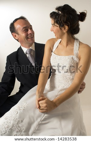 A newly wed couple stare at each other, smiling, while the wife is sitting on the husbands lap. - vertically framed