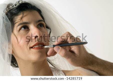 A woman getting a red shade of lip liner on her lips. She is preparing to get married. - horizontally framed