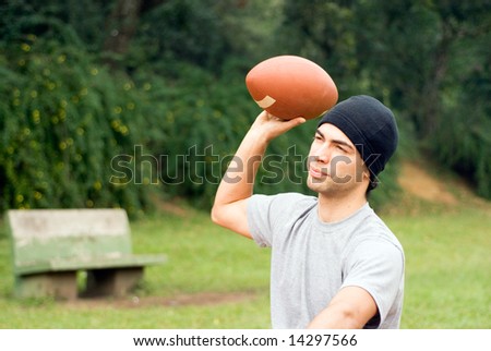 A man, sitting, ready to throw a football, at a park. - horizontally framed