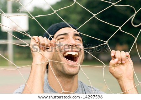 A man playing with a soccer goal net, screaming and laughing through it, while holding onto it. - horizontally framed