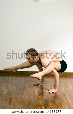 Man performing yoga. Arms supporting body, legs and feet draped over shoulders. Vertically framed shot.