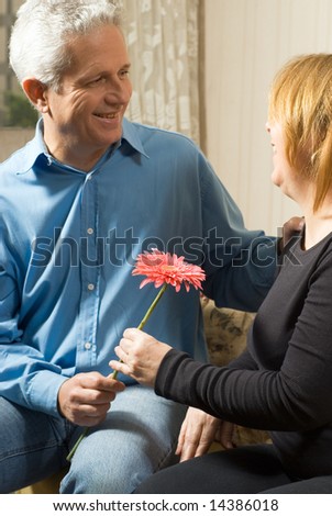 A couple staring at each other, holding a pink flower, smiling. - vertically framed
