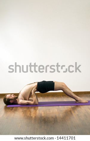 Man performing yoga on mat. Lying on shoulders, feet on ground, arms supporting back. Vertically framed shot.