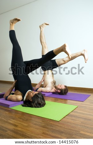 Man and woman performing yoga together on mats. Lying on shoulders, feet in air above head, legs spread. Vertically framed shot.