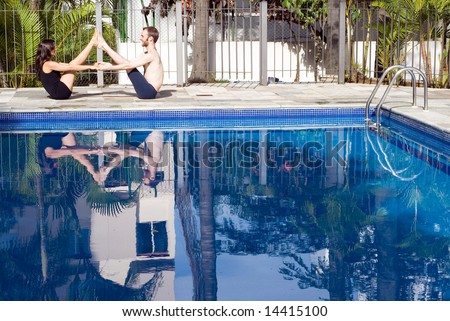 A couple, with their feet together and hands together, stretch with each other next to the pool - horizontally framed