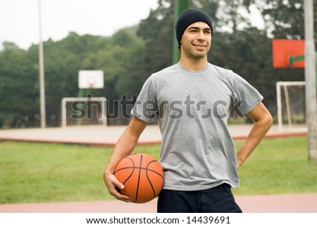 A man, standing tall, holding a basketball by his side, posing for the camera - horizontally framed