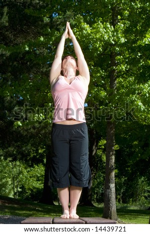 Woman standing on picnic table in the park. Posed in yoga position, head back, arms above head in prayer formation. Vertically framed shot.