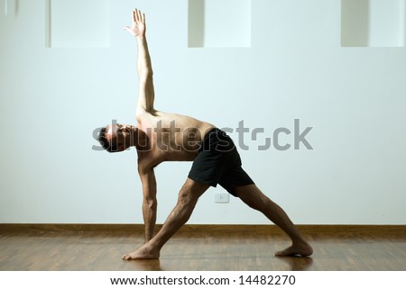 Man in a yoga pose with one arm extended up and the other down and his legs apart. Horizontally framed photograph