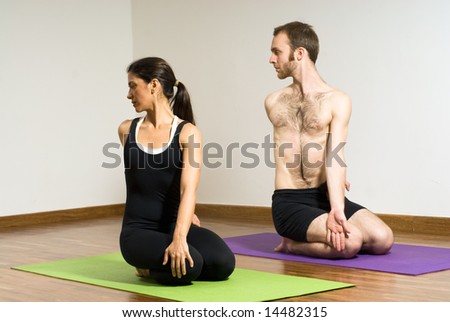 Man and Woman on yoga mats on their knees with their bodies turned backwards. Horizontally framed photograph