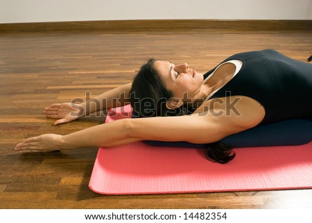 Woman lying on a yoga mat with her arms extended above her head and her eyes closed. Horizontally framed photograph