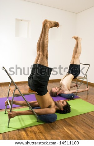 Two men balance themselves using stools and ladders. Vertically framed photograph.