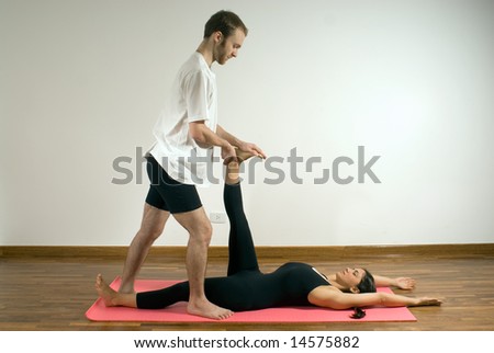 Man and woman in a yoga pose, he is standing as he pushes her leg back. - Horizontally framed photograph