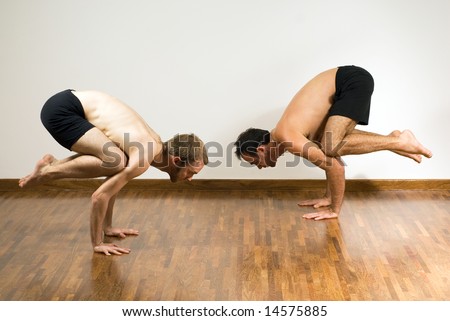 Two men in a balancing pose. They are crouched on their hands with their feet in the air. Horizontally framed photograph.