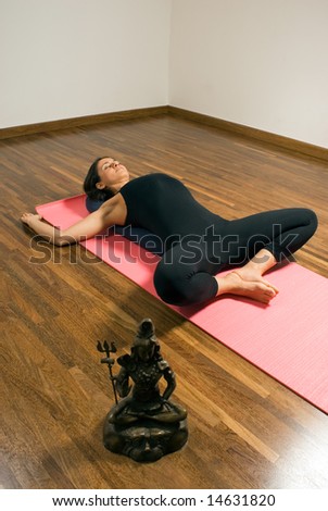 Woman lying on a pink yoga mat with her legs crossed next to a bronze statue. Vertically framed photograph