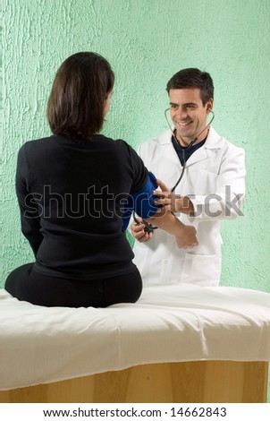 A young male doctor, checks a patients blood pressure while he listens to her pulse. - vertically framed