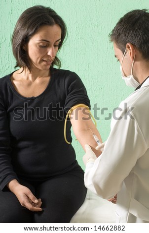 A male doctor is giving his female patient a shot.  The doctor and the patient are both looking at the syringe.  Vertically framed photo.