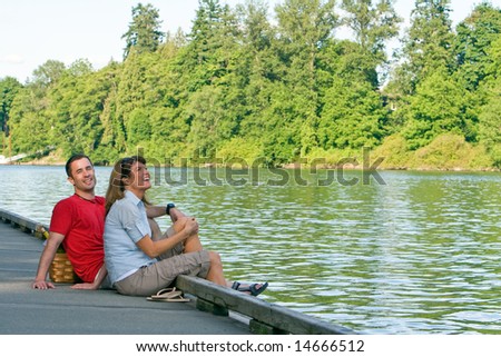 A couple, sitting together on a dock, with their feet dangling over into the water, laughing. - horizontally framed
