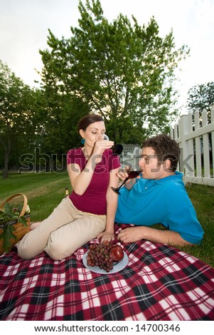 A young couple, lie and sit down together, having a picnic, drinking. - vertically framed