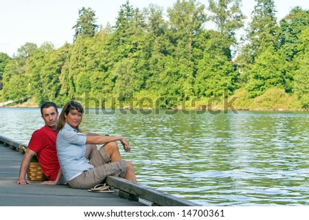 A couple, sit together on a dock, with their feet dangling over. - horizontally framed