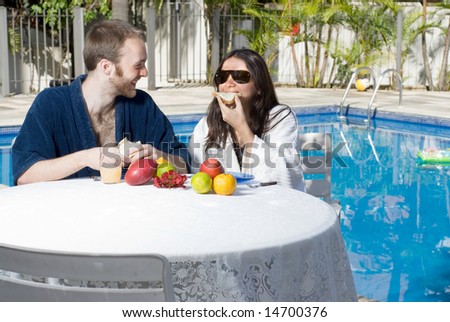 A young, attractive couple, eats fruits. The man sits down in a black robe, and the woman sits next to him in a white robe, eating. - horizontally framed