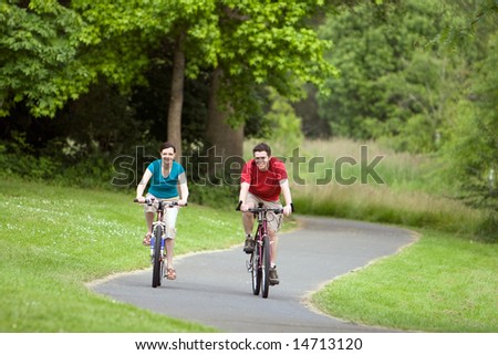 A man and woman, ride their bicycles along a park trail happily. - horizontally framed