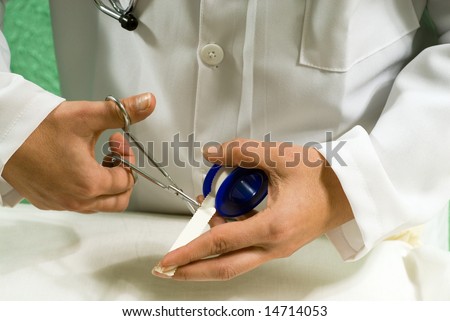 A doctor is cutting medical tape with scissors in his office.  Horizontally framed photo.
